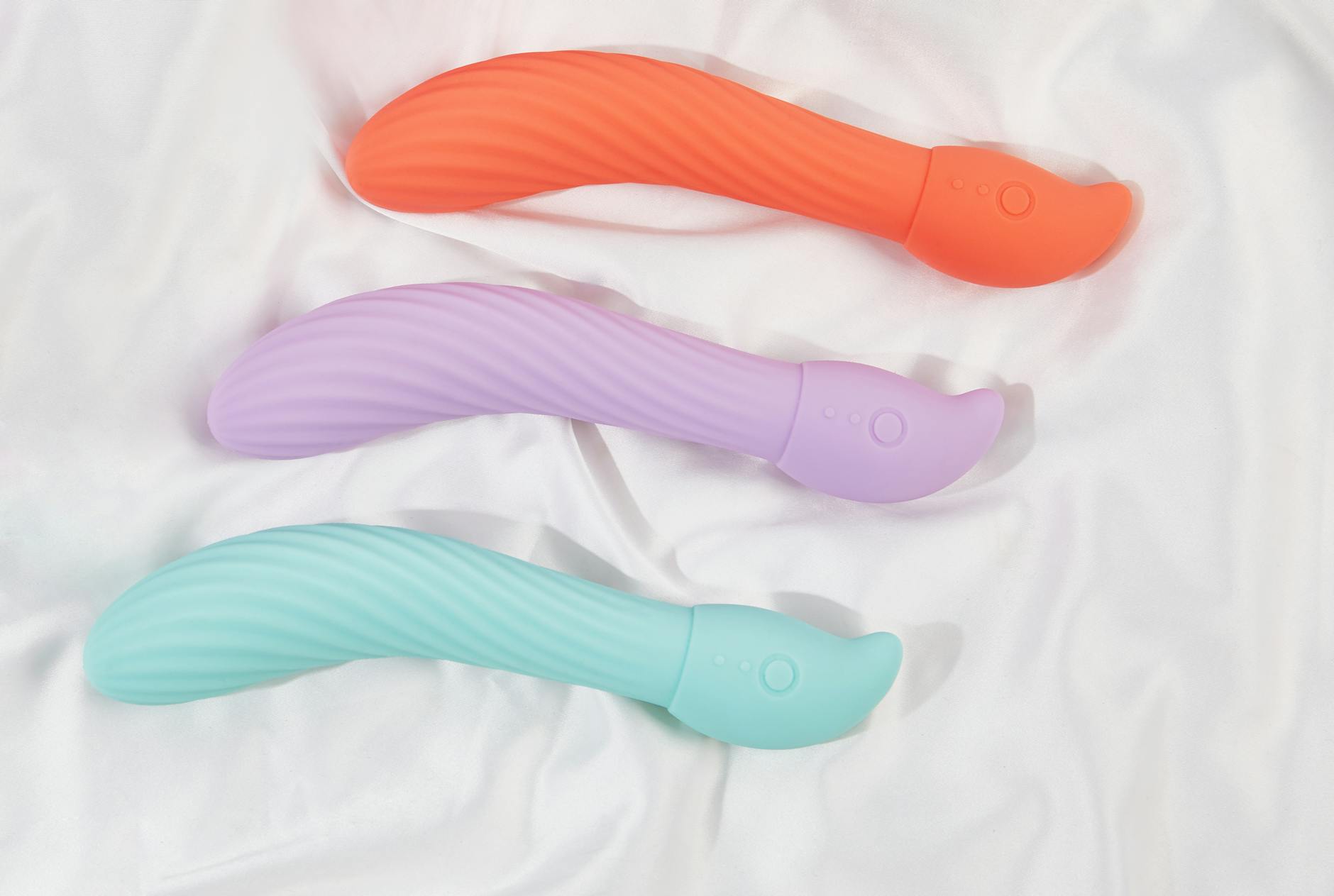 Three colorful vibrators arranged on white fabric, showing their smooth contours