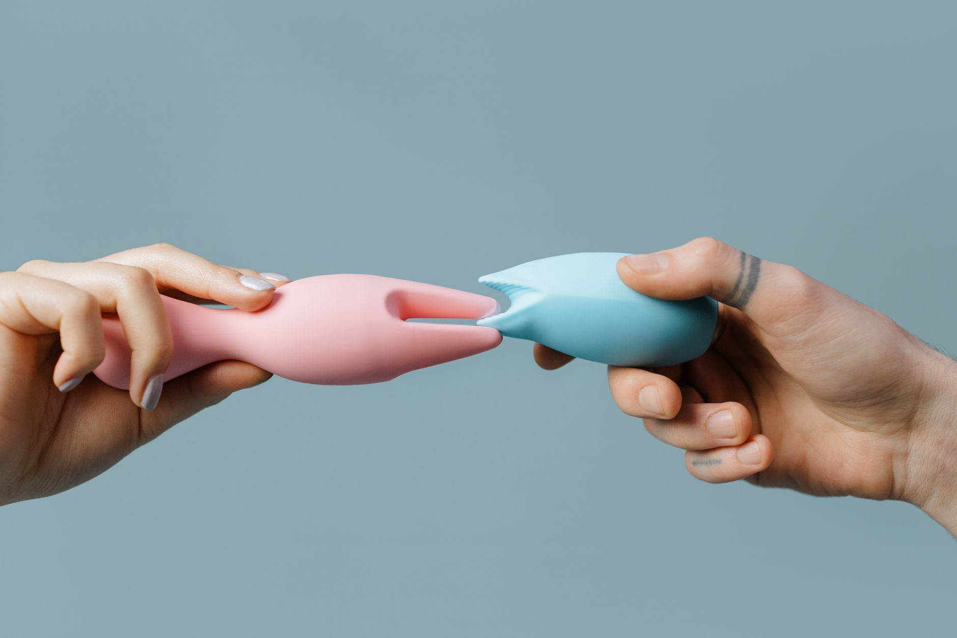 Hands holding pastel-colored silicone lemon clitoral vibrators against a soft background