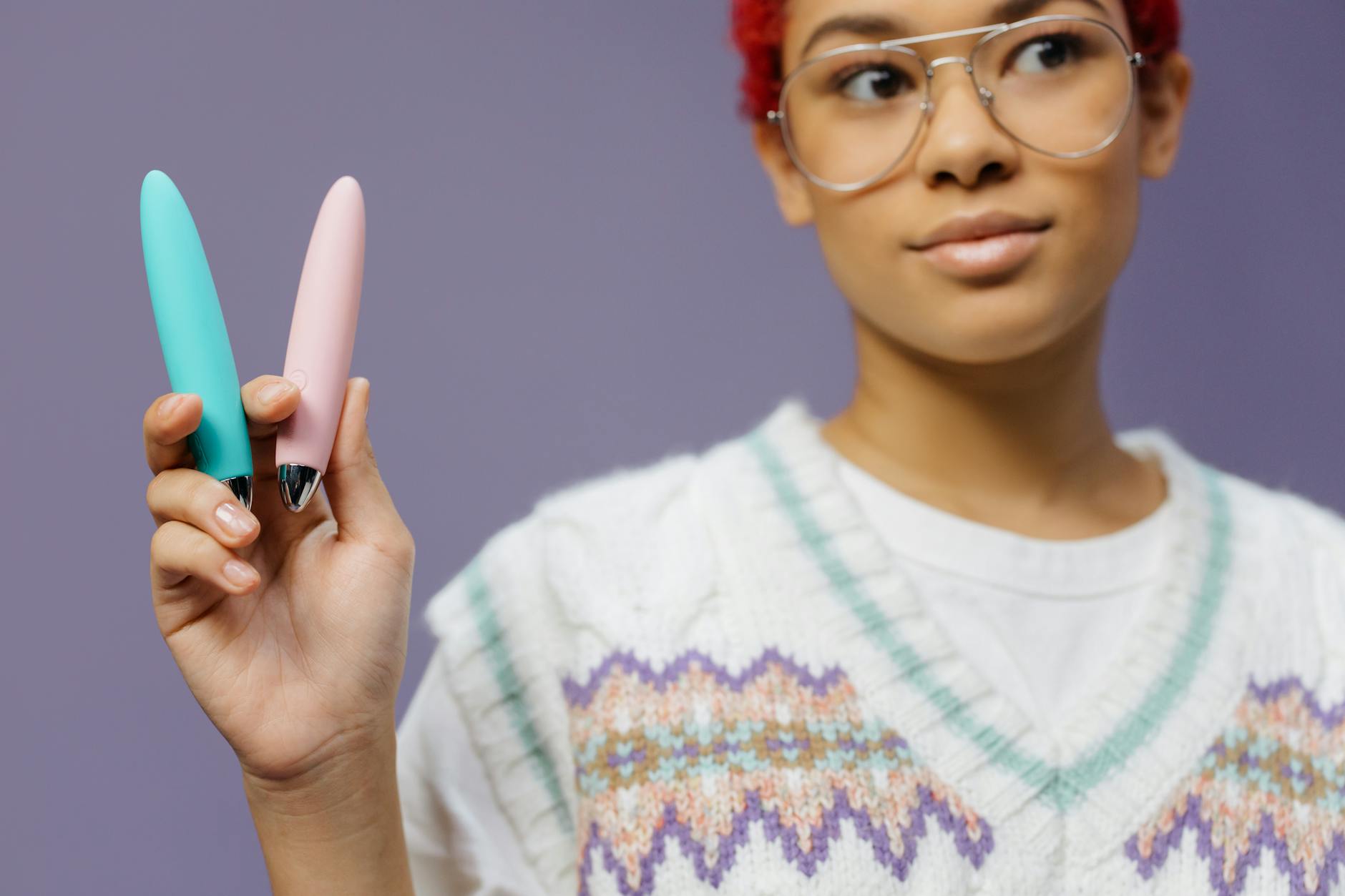 A woman holding two colorful clitoral vibrators against a purple background