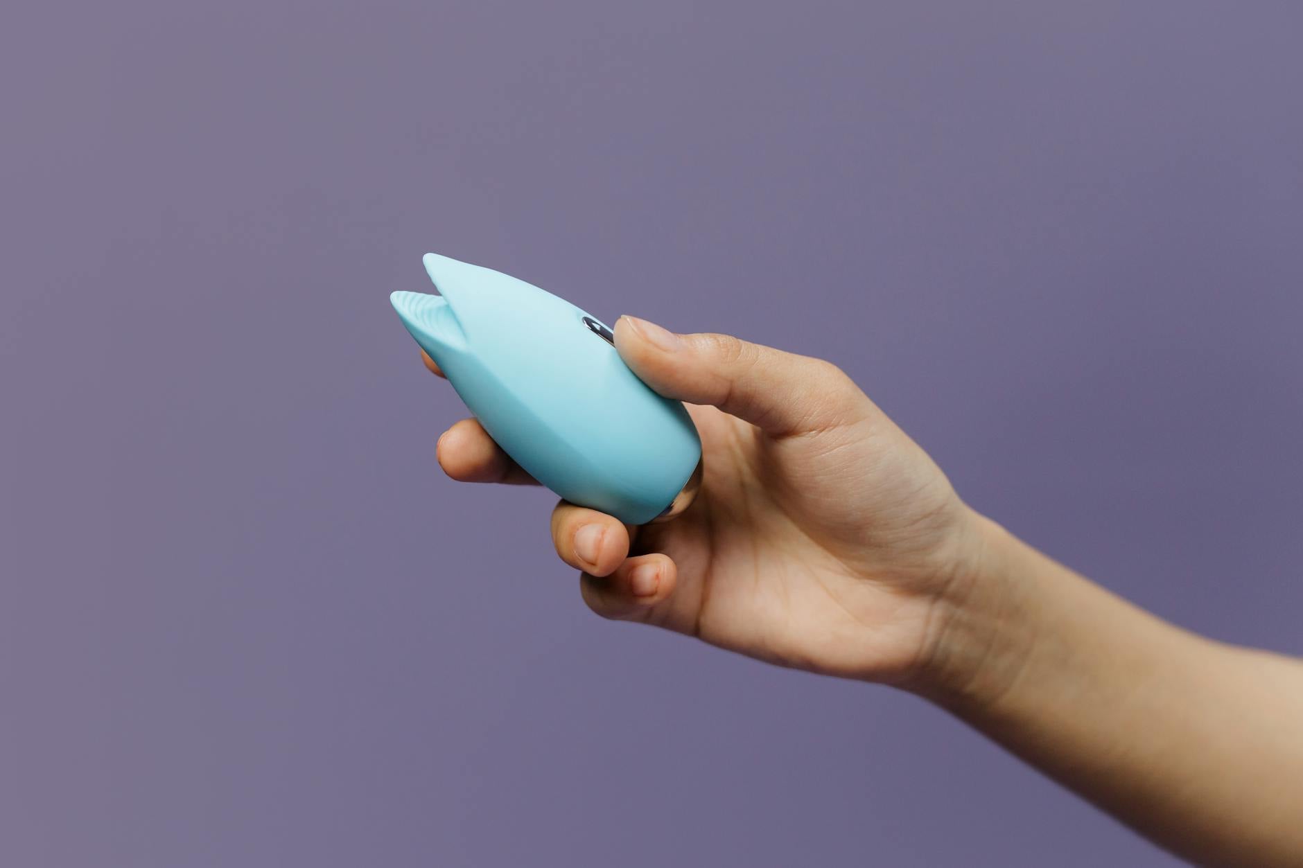 A silicone vibrator held in hand against a purple background, symbolizing self-pleasure and intimate connection